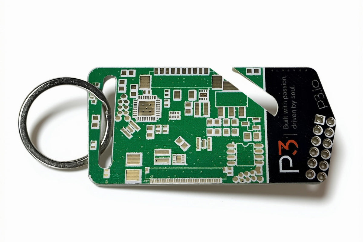 A green circuit board keychain tool with a silver metal key ring and a black branded end cap, photographed on a clean white background.