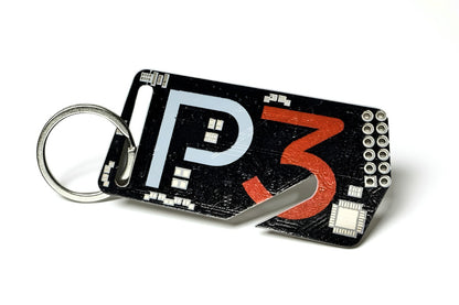 A black rectangular keychain tool with a silver split ring, featuring a stylized 'P3' design in white and orange, with a small built-in slot at the bottom right, shown on a white background.