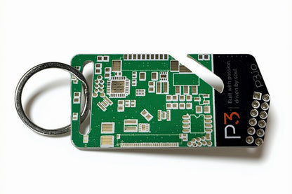 A green circuit board keychain tool with a silver metal key ring and a black branded end cap, photographed on a clean white background.